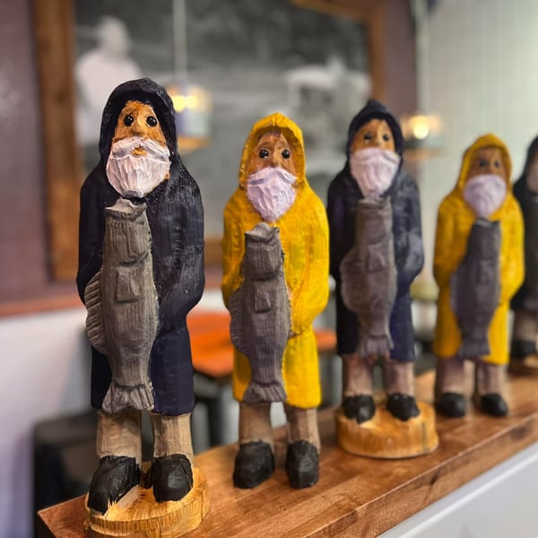 Wooden fisherman figurines with beards and fish, some wearing face masks, displayed on a wooden shelf.
