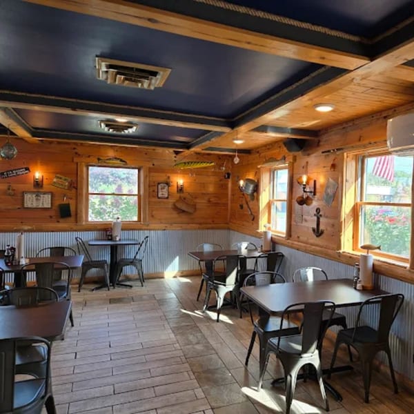A rustic restaurant interior with wooden walls, dark blue ceiling, and black tables and chairs.