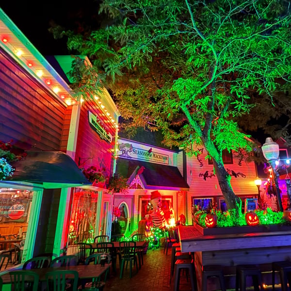 A vibrant outdoor dining area at night, illuminated with colorful Halloween decorations and string lights.