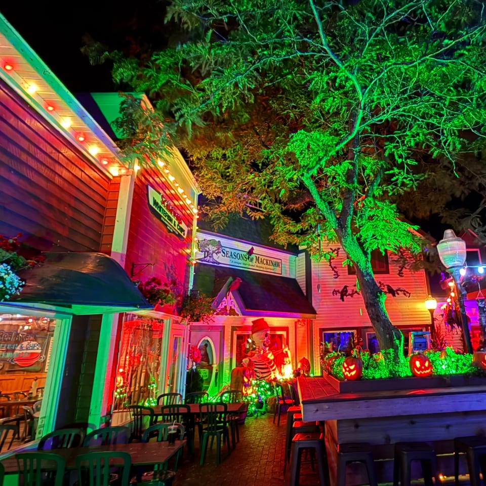 A vibrant outdoor dining area at night, illuminated with colorful Halloween decorations and string lights.
