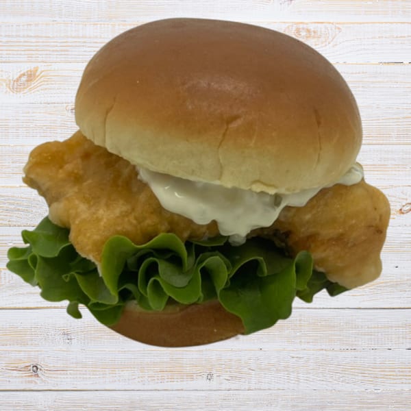 Crispy fried fish sandwich with lettuce and tartar sauce on a bun, against a white wooden background.