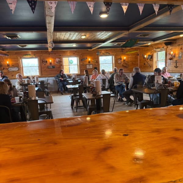 A rustic restaurant interior with wooden walls, nautical decor, and patrons seated at tables.