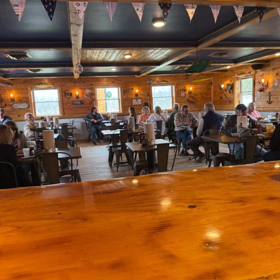 A rustic restaurant interior with wooden walls, nautical decor, and patrons seated at tables.