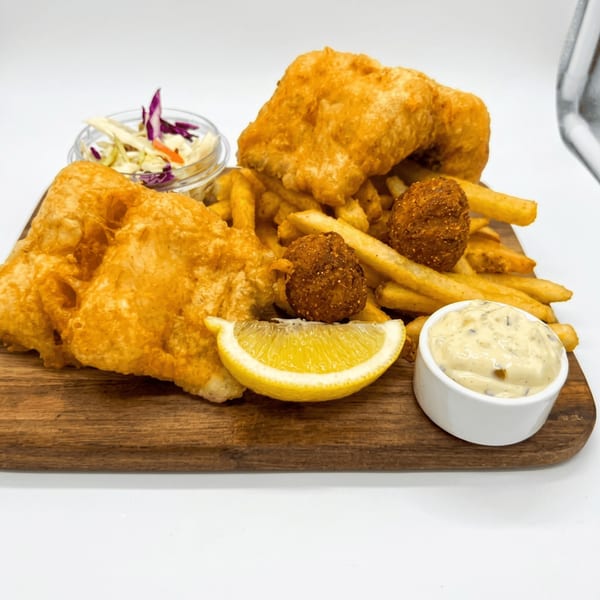 Golden fried fish and chips with hush puppies, coleslaw, lemon, and tartar sauce on a wooden board.