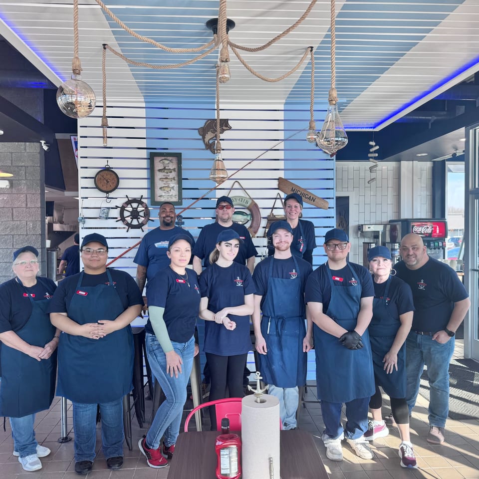 Eleven restaurant staff members in blue uniforms and aprons pose together in a brightly lit dining area.
