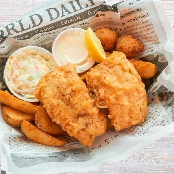 Golden fried fish and chips with coleslaw, tartar sauce, and hushpuppies served on newspaper.
