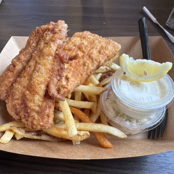 Golden-brown fish and chips in a cardboard tray with tartar sauce and a lemon wedge.