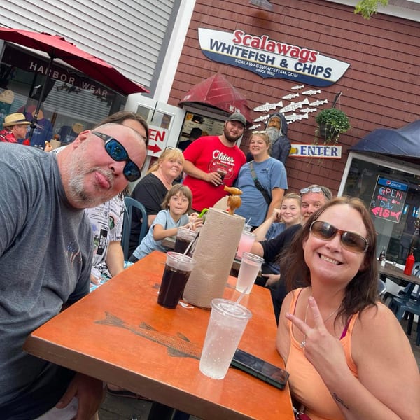 A group of people smiling and posing for a photo at an outdoor restaurant, Scalawags Whitefish & Chips.